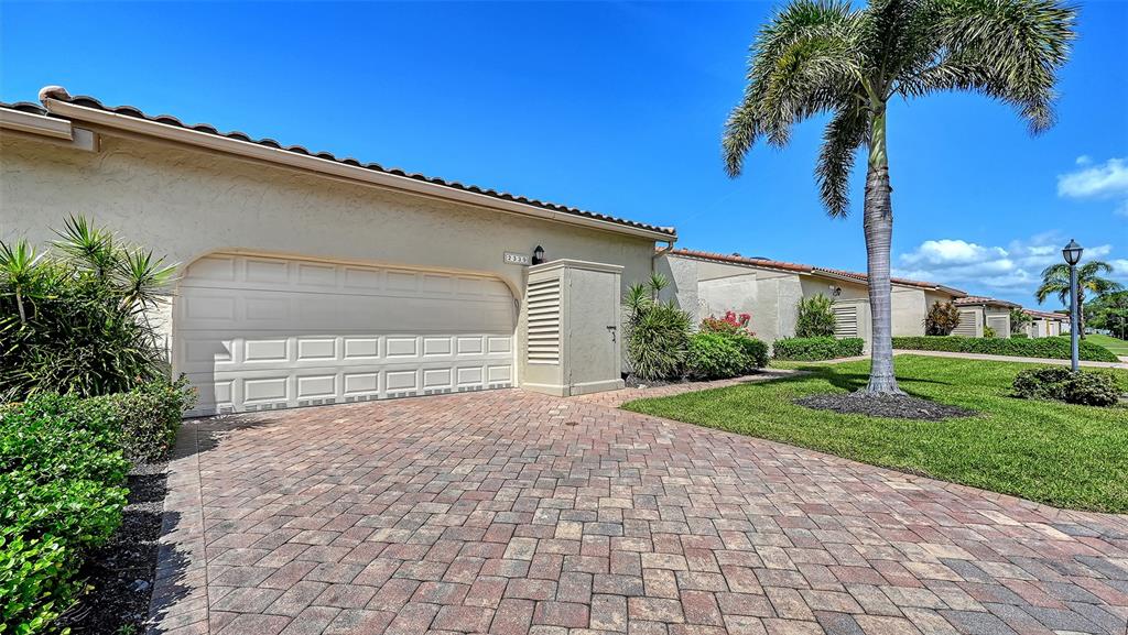 A beige house with a two-car garage and a paved driveway under a blue sky — 2339 HARBOUR OAKS DRIVE, LONGBOAT KEY, FL