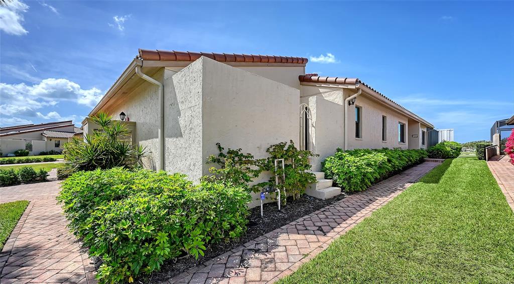 A beige stucco house features a tiled roof, brick walkway, and lush green landscaping — 2339 HARBOUR OAKS DRIVE, LONGBOAT KEY, FL