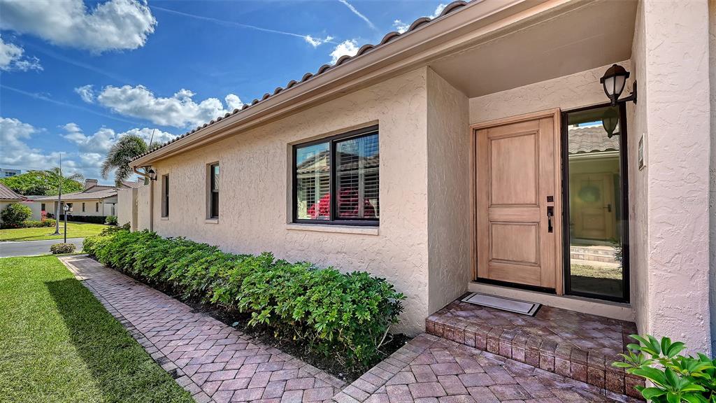A beige stucco house exterior features a wooden front door, brick walkway, and green landscaping — 2339 HARBOUR OAKS DRIVE, LONGBOAT KEY, FL
