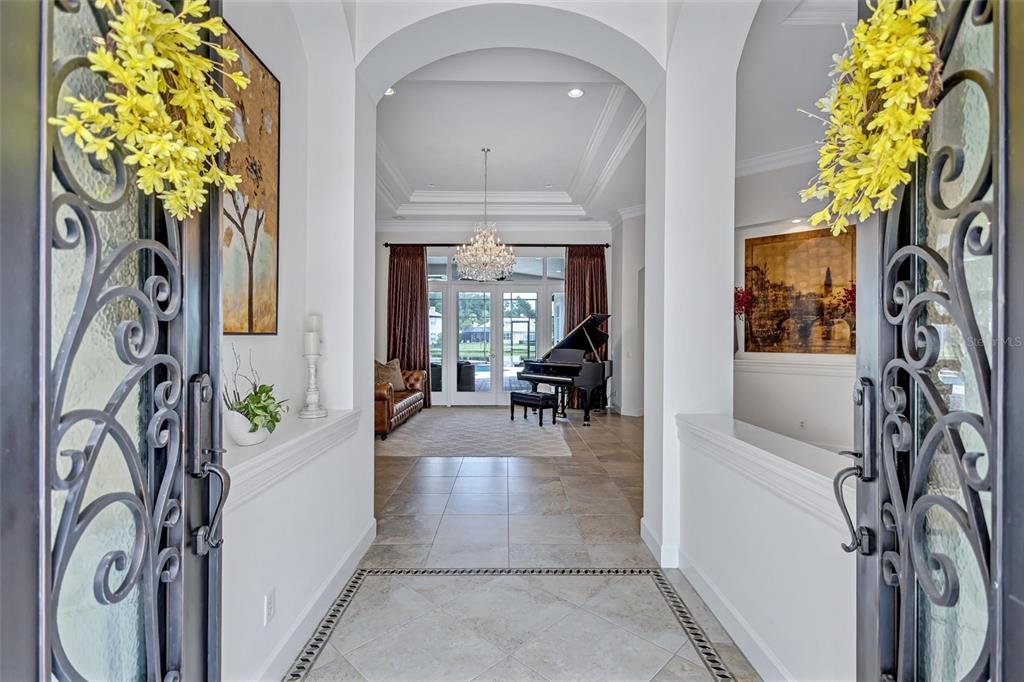 A view through an ornate iron door into a tiled foyer with a grand piano — 14742 WATERCHASE BOULEVARD, TAMPA, FL