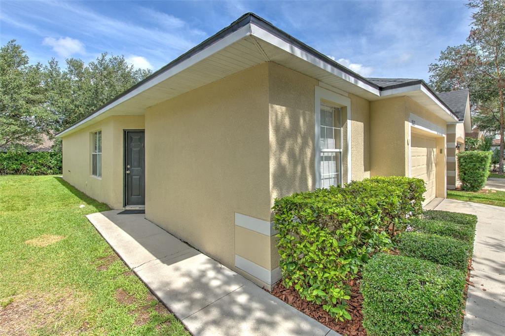 A tan stucco house exterior features a dark front door, a window, and manicured hedges — 5843 WRENWATER, LITHIA, FL