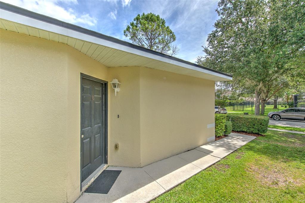 A beige exterior wall with a dark door and a concrete walkway under a roof — 5843 WRENWATER, LITHIA, FL