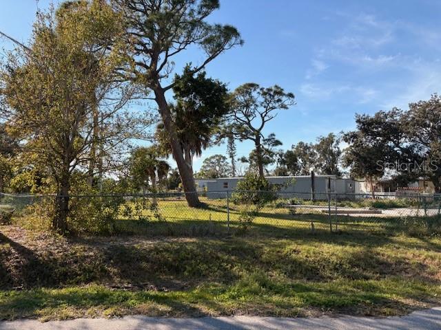 A chain-link fence encloses a grassy lot with several trees and a distant mobile home — 1431 COLONIA LANE E, NOKOMIS, FL
