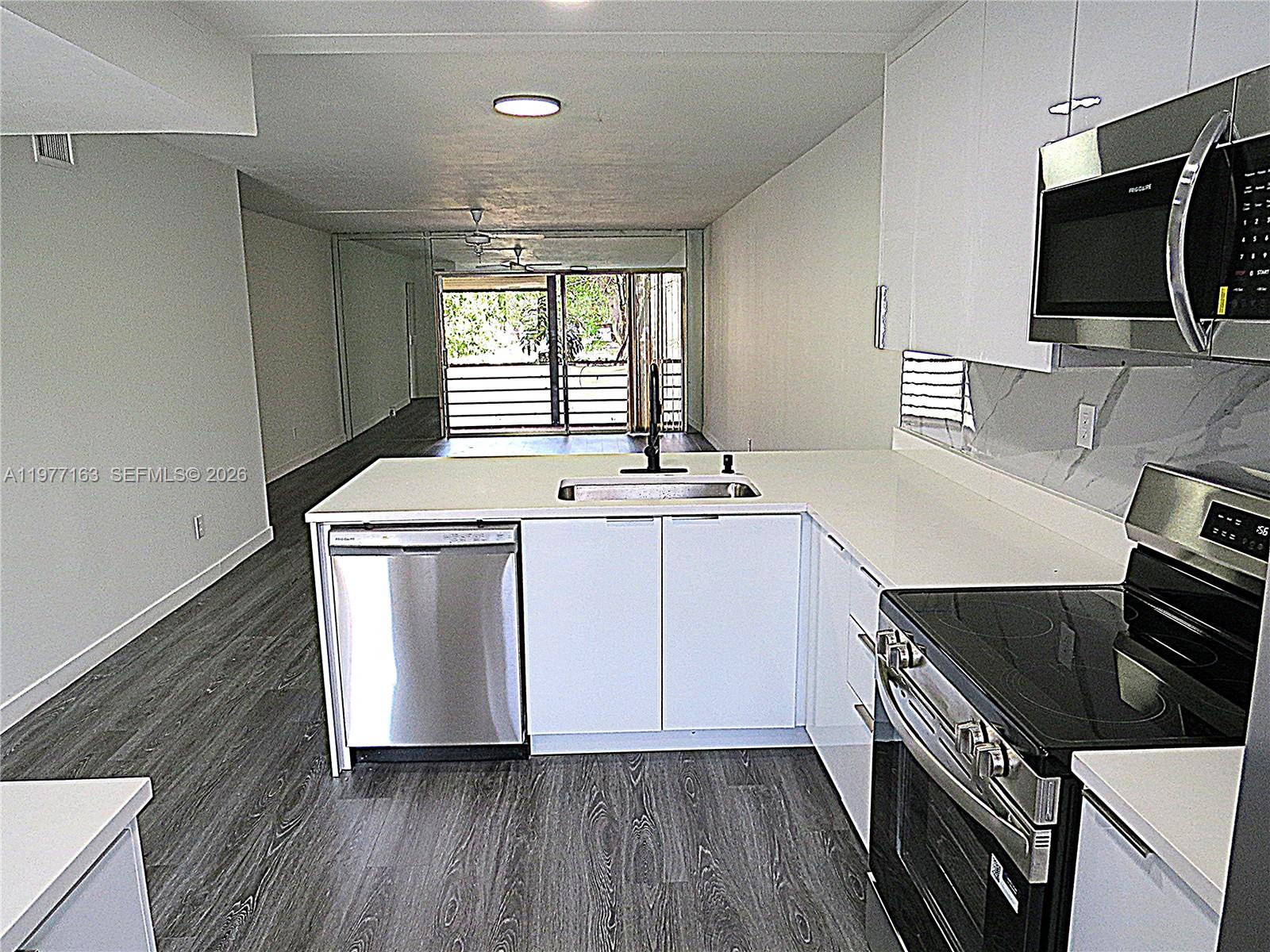 A modern kitchen with white cabinets and stainless steel appliances overlooks an open living area — 3591 Inverrary Dr # 203, Lauderhill FL 33319, LAUDERHILL, FL