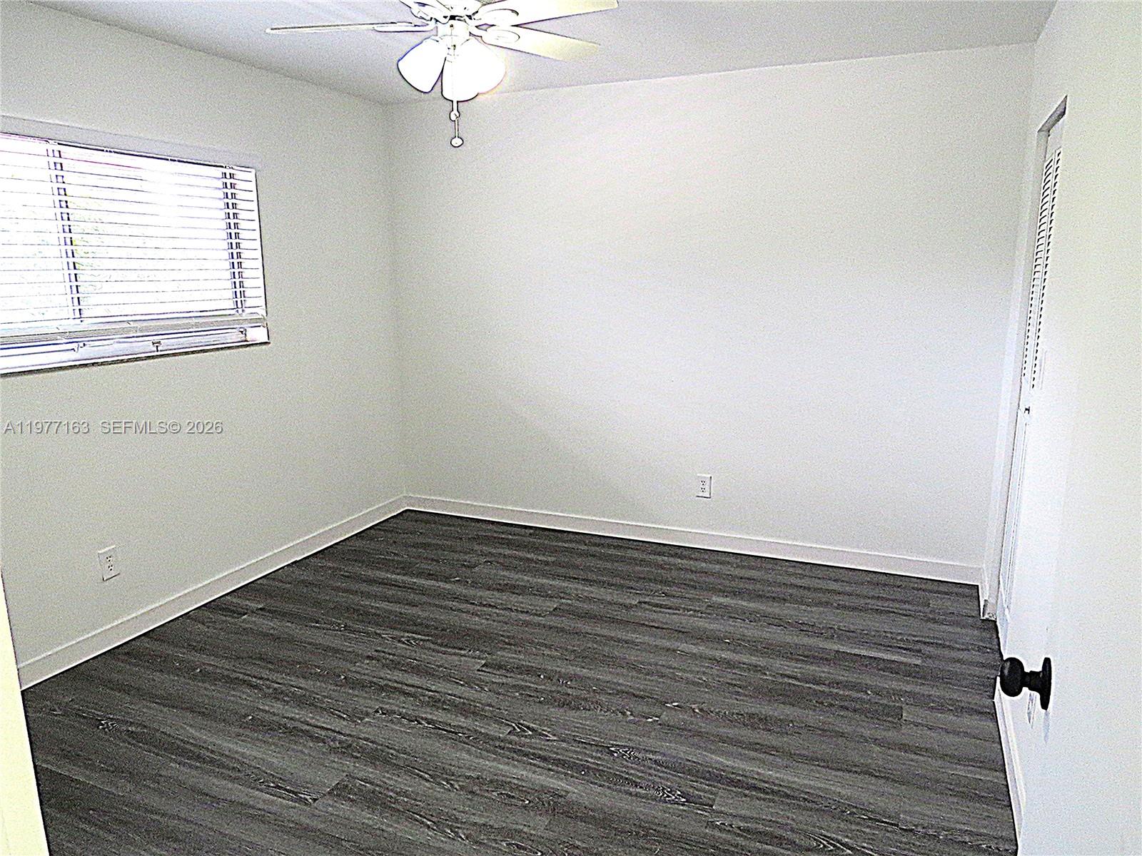 An empty bedroom features white walls, dark wood-look flooring, a ceiling fan, and a window — 3591 Inverrary Dr # 203, Lauderhill FL 33319, LAUDERHILL, FL