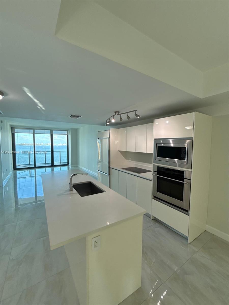 A modern kitchen features white cabinetry, a central island with a sink, and floor-to-ceiling windows — 460 NE 28th St # 1907, Miami FL 33137, MIAMI, FL