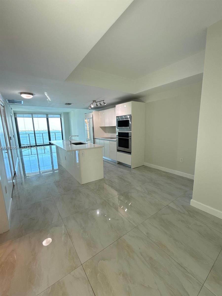 A modern kitchen features white cabinetry, a central island, and large light-colored floor tiles — 460 NE 28th St # 1907, Miami FL 33137, MIAMI, FL