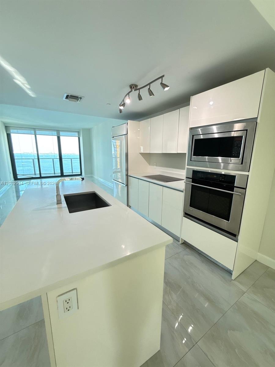 A modern kitchen features white cabinetry, stainless steel appliances, and a central island with sink — 460 NE 28th St # 1907, Miami FL 33137, MIAMI, FL