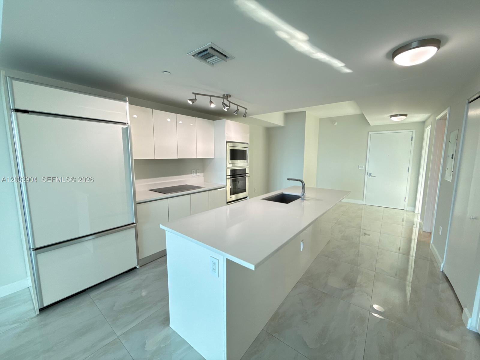 A modern kitchen features white cabinetry, a central island with a sink, and tiled floors — 460 NE 28th St # 1907, Miami FL 33137, MIAMI, FL