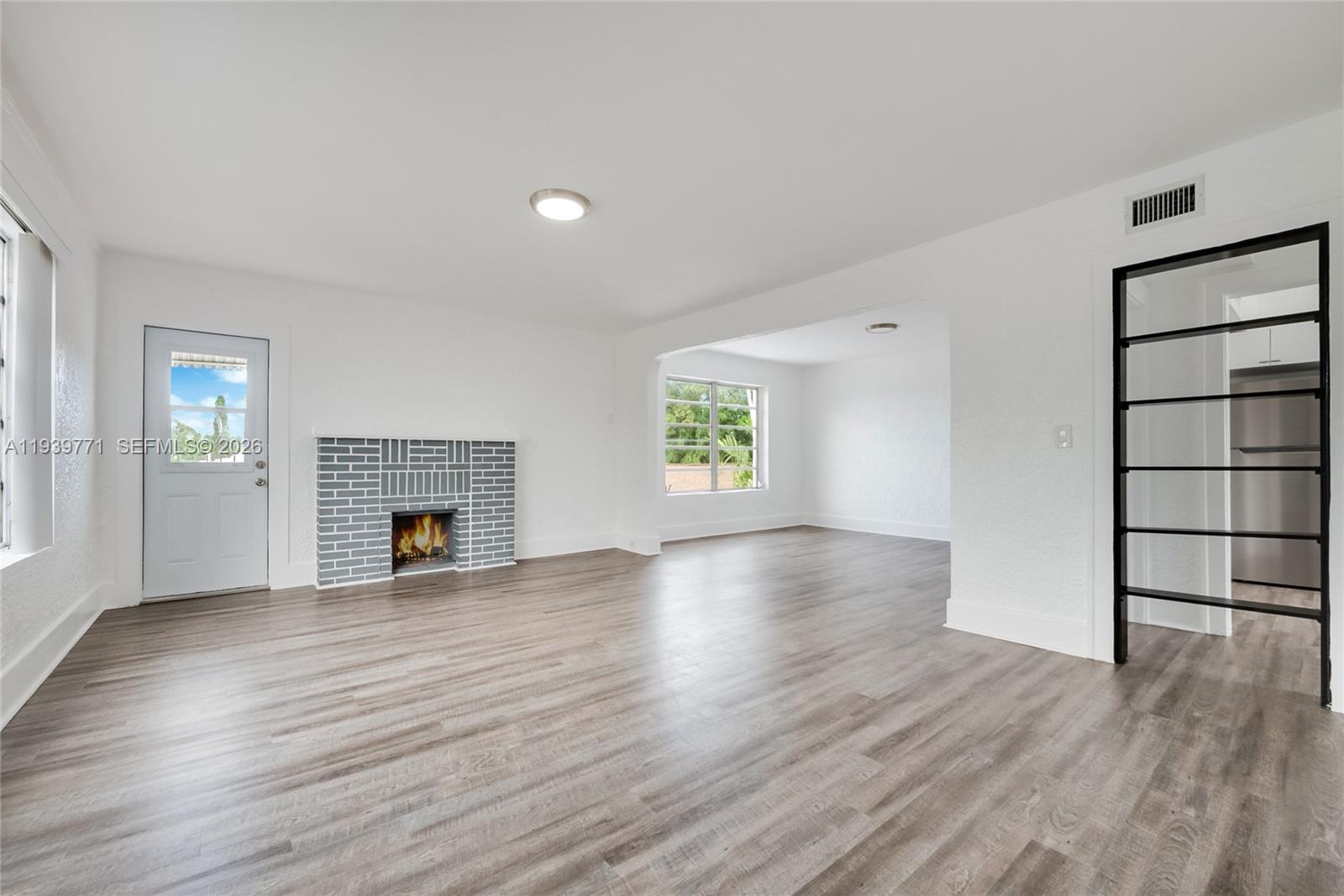 A living room features white walls, gray wood-look flooring, a brick fireplace, and a doorway — 1736 SW 9th St, Miami FL 33135, MIAMI, FL