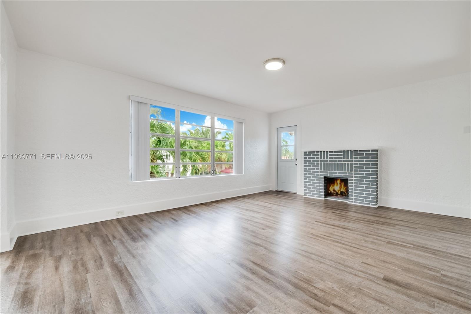 A living room features wood-look flooring, white walls, a large window, and a gray fireplace — 1736 SW 9th St, Miami FL 33135, MIAMI, FL