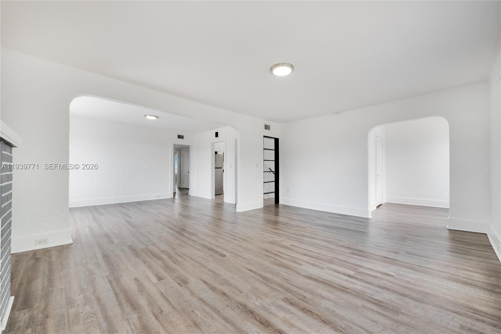An empty living area features white walls, arched doorways, and light wood-look flooring — 1736 SW 9th St, Miami FL 33135, MIAMI, FL