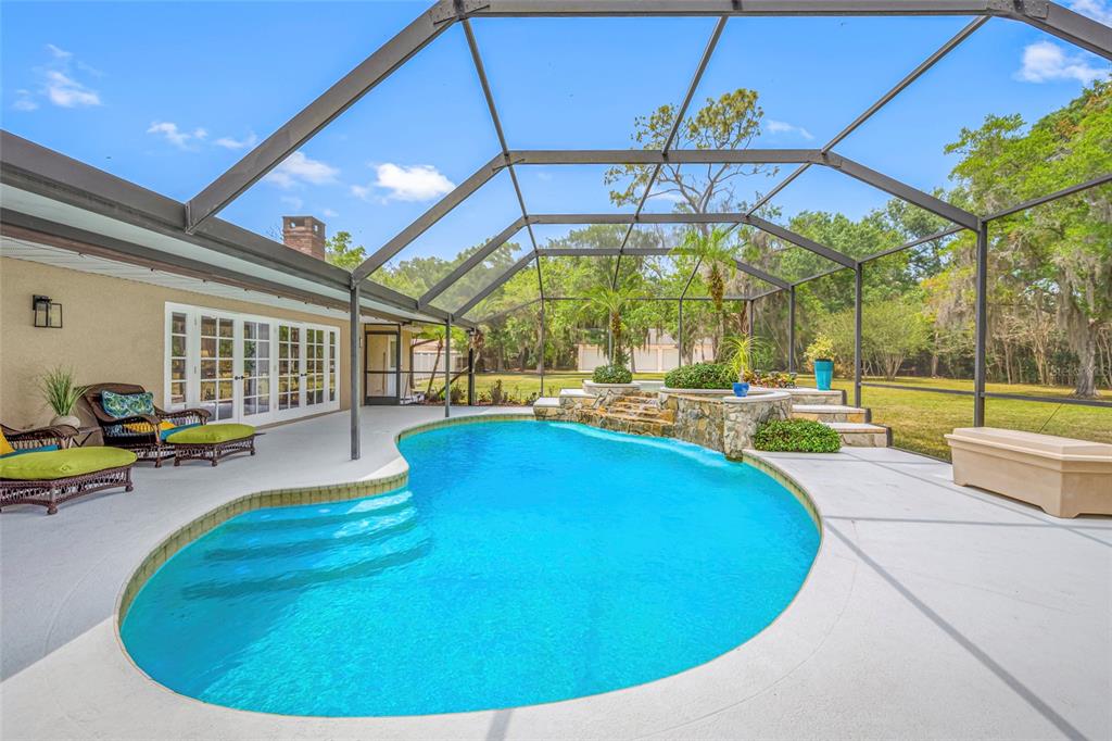 A screened-in patio features a kidney-shaped swimming pool with a stone waterfall and steps — 15314 LAKE MAGDALENE BOULEVARD, TAMPA, FL