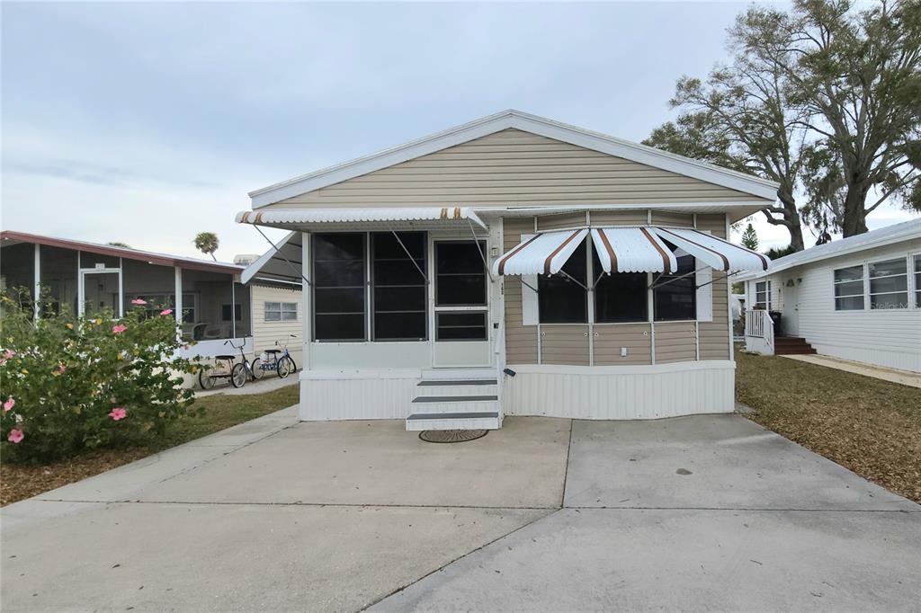 A single-story manufactured home with a concrete driveway, screened front porch, and white metal awnings — 3275 26TH AVENUE E UNIT 160, BRADENTON, FL