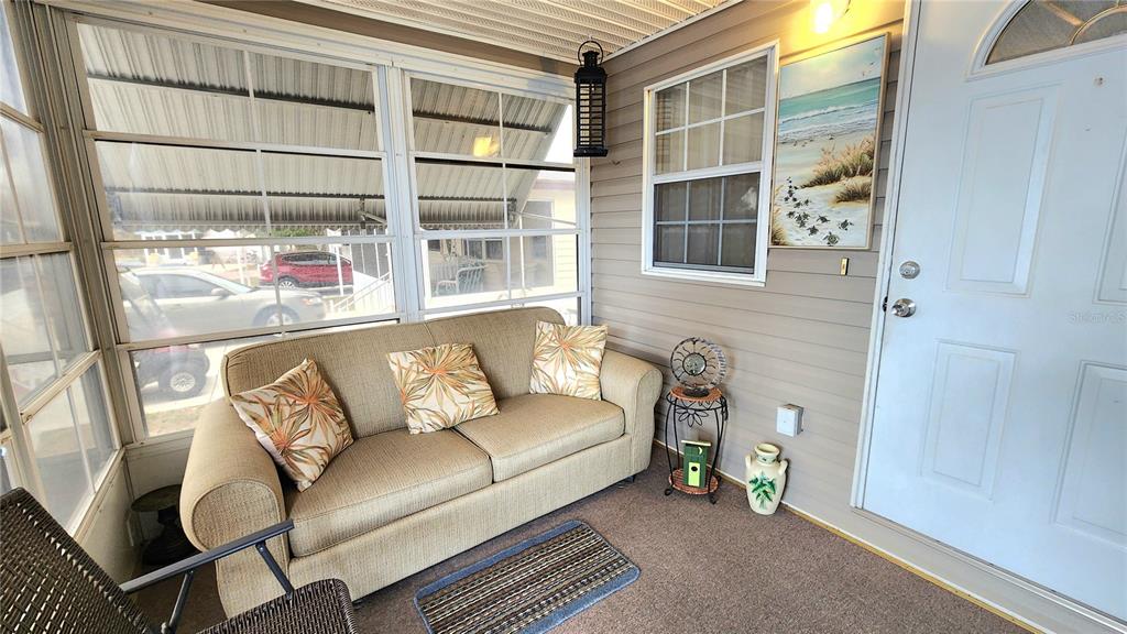 A sunroom features a beige sofa, a small side table, and a white entry door — 3275 26TH AVENUE E UNIT 160, BRADENTON, FL