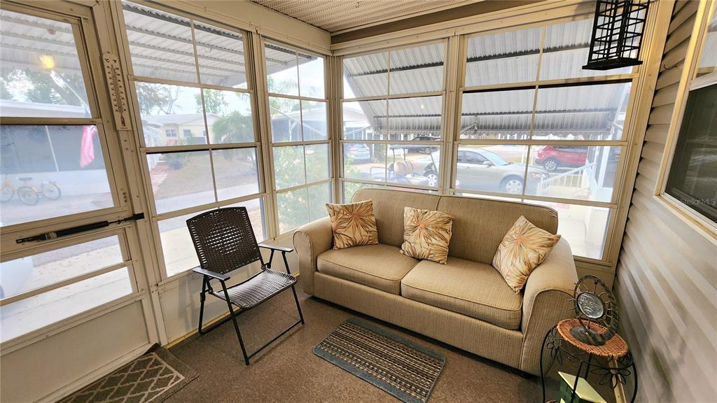 A sunroom features a beige sofa, a folding chair, and large windows overlooking a parking area — 3275 26TH AVENUE E UNIT 160, BRADENTON, FL