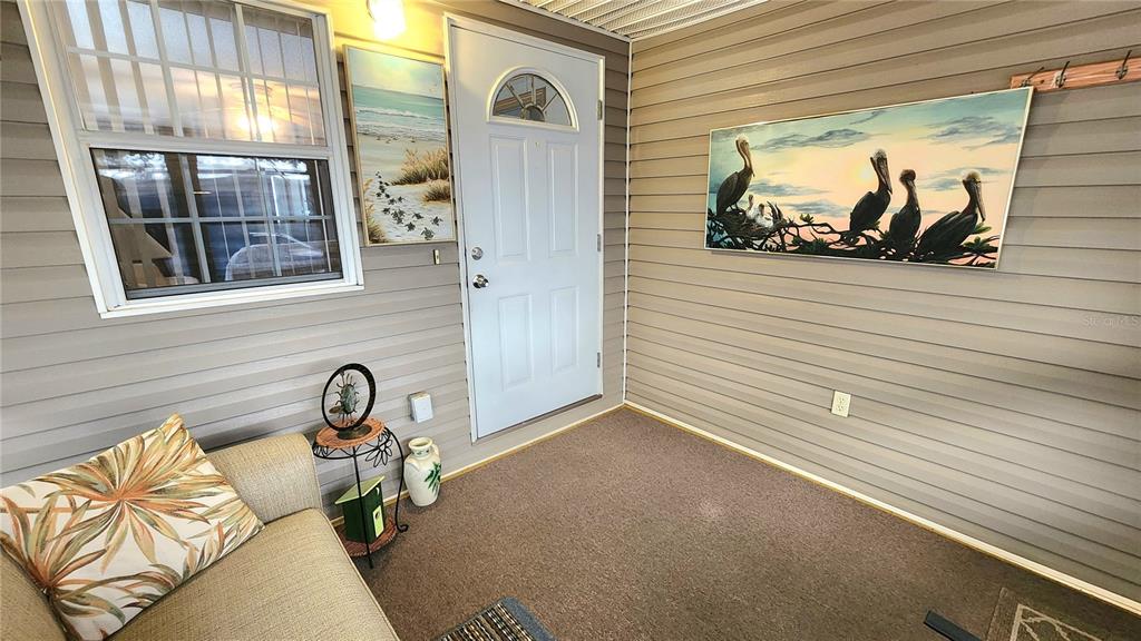 A sunroom features gray horizontal siding, a white door, a sofa, and coastal wall art — 3275 26TH AVENUE E UNIT 160, BRADENTON, FL