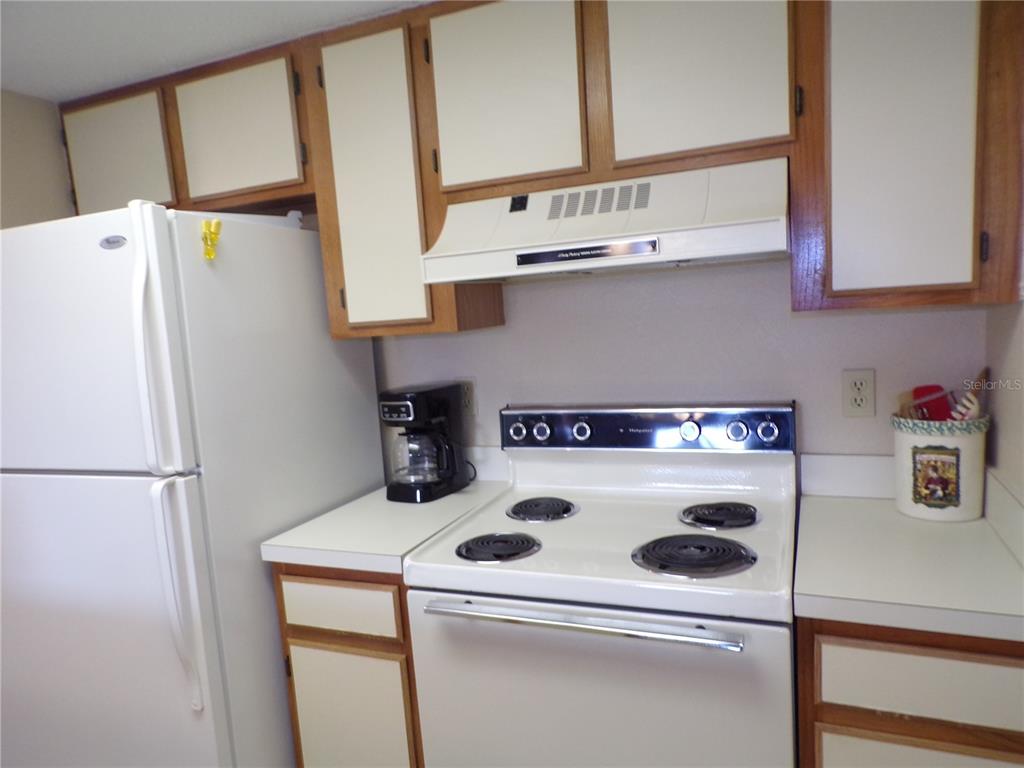 A kitchen features white appliances, wood-trimmed cabinets, and white countertops — 4016 OAKVIEW DRIVE UNIT J9, PORT CHARLOTTE, FL