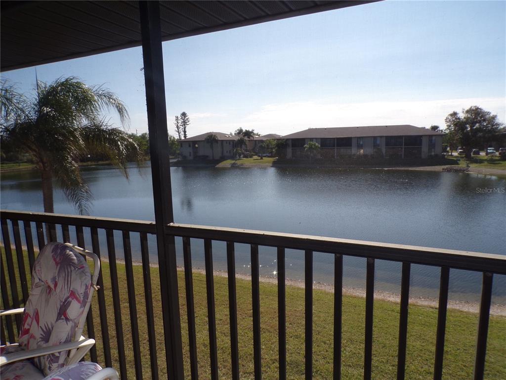 A view of a lake and apartment buildings from a screened-in balcony with railings — 4016 OAKVIEW DRIVE UNIT J9, PORT CHARLOTTE, FL