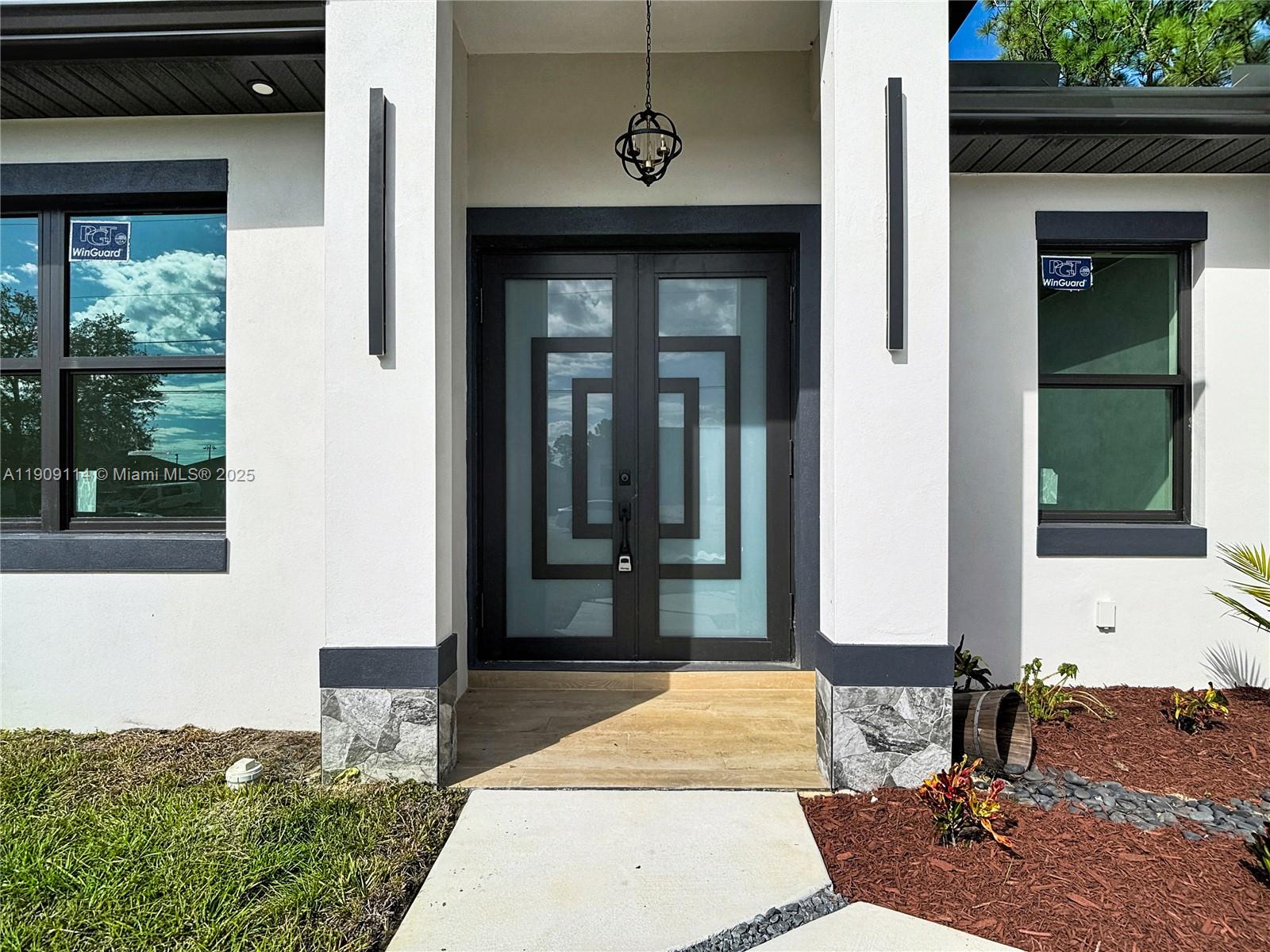 The exterior of a modern home features a double glass door with geometric frames — 3814 9th St SW, Lehigh Acres FL 33976, LEHIGH ACRES, FL