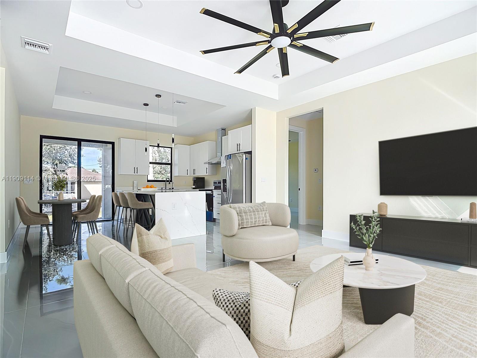 An open-concept living room and kitchen feature a large ceiling fan and white cabinetry — 3814 9th St SW, Lehigh Acres FL 33976, LEHIGH ACRES, FL