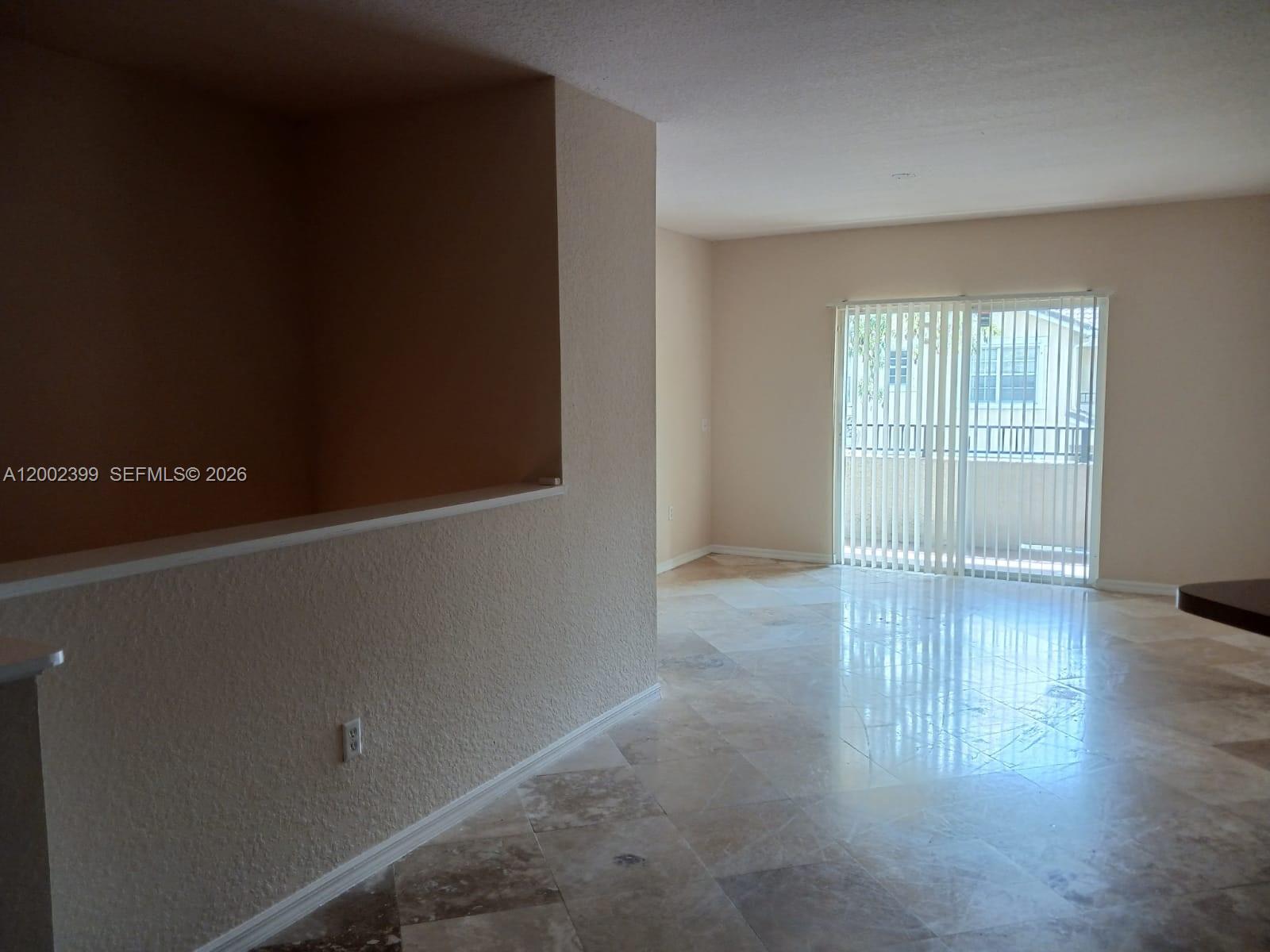An empty room features beige walls, tile flooring, and a sliding glass door to a balcony — NORTH LAUDERDALE, FL