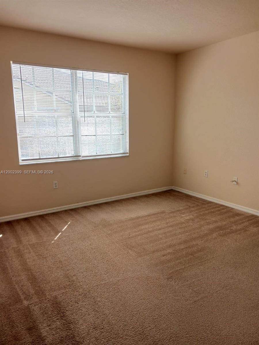 An empty bedroom features beige walls, tan carpeting, and a window with white blinds — NORTH LAUDERDALE, FL