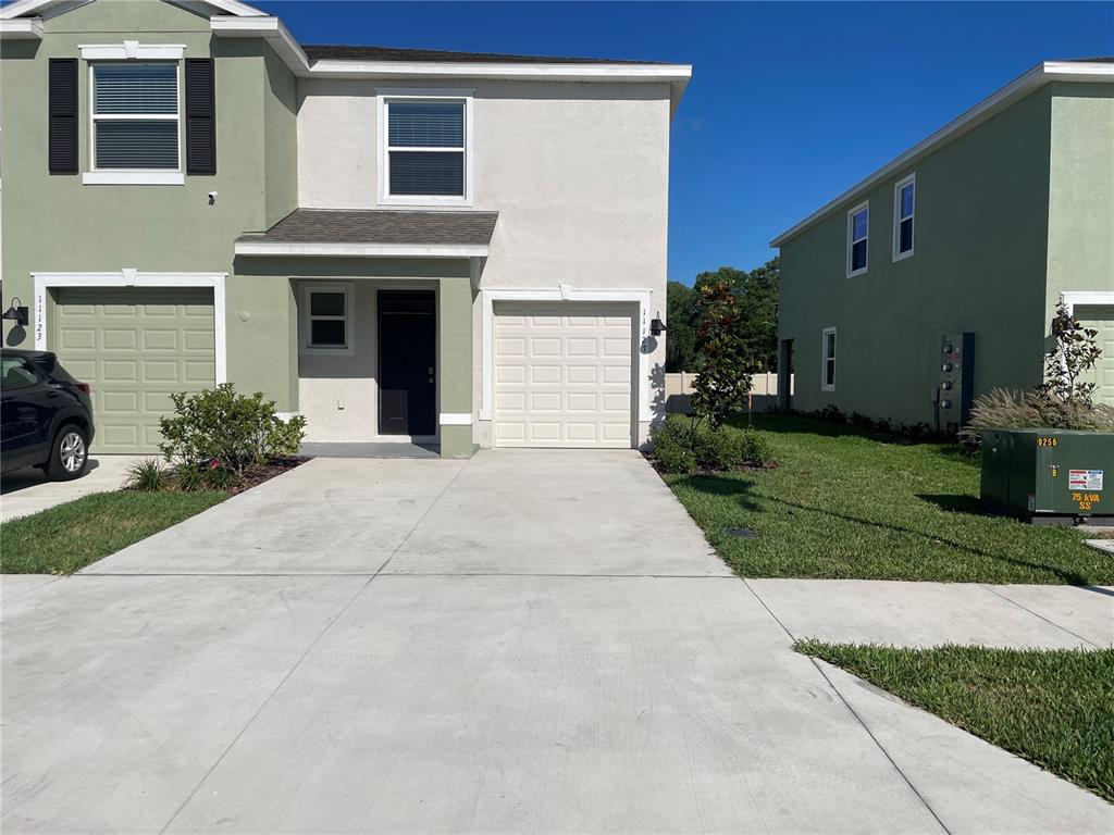 A two-story townhouse with a light-colored facade, a single-car garage, and a concrete driveway — 11127 CRESCENT DEER DRIVE, LAND O LAKES, FL