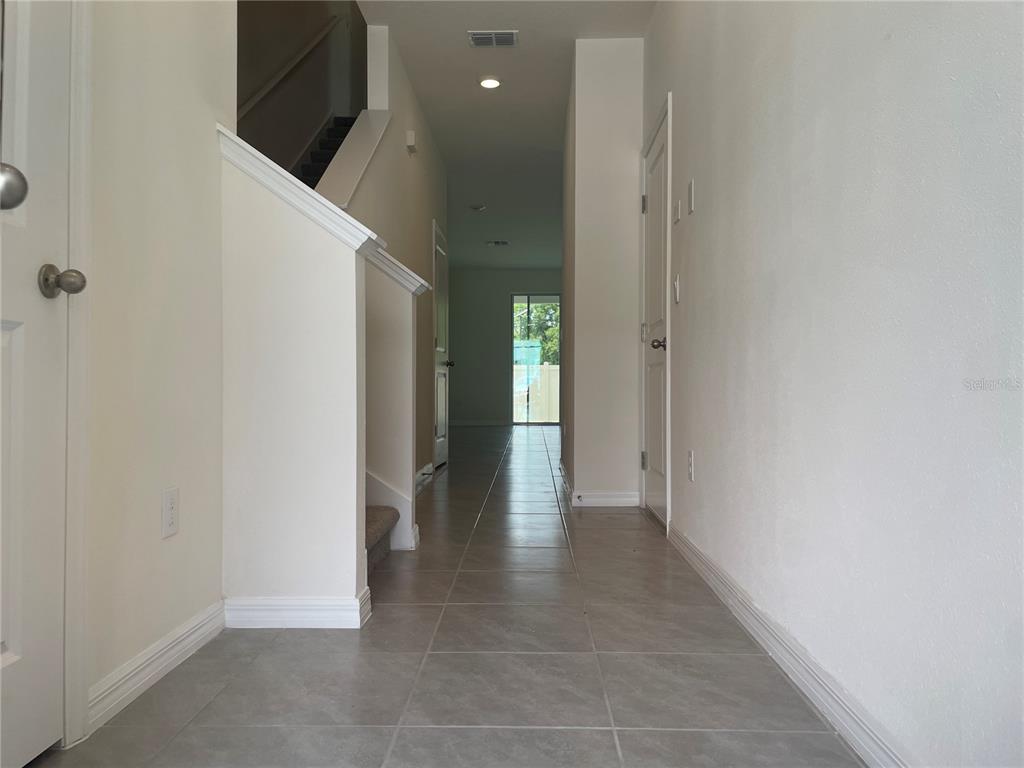 A tiled hallway leads past a staircase and closed doors toward a rear glass door — 11127 CRESCENT DEER DRIVE, LAND O LAKES, FL