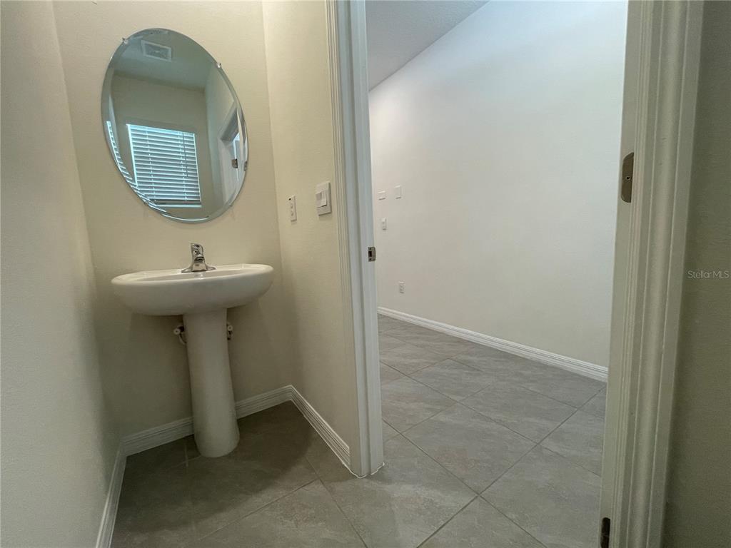 A small bathroom with a pedestal sink and oval mirror opens into an adjacent room — 11127 CRESCENT DEER DRIVE, LAND O LAKES, FL