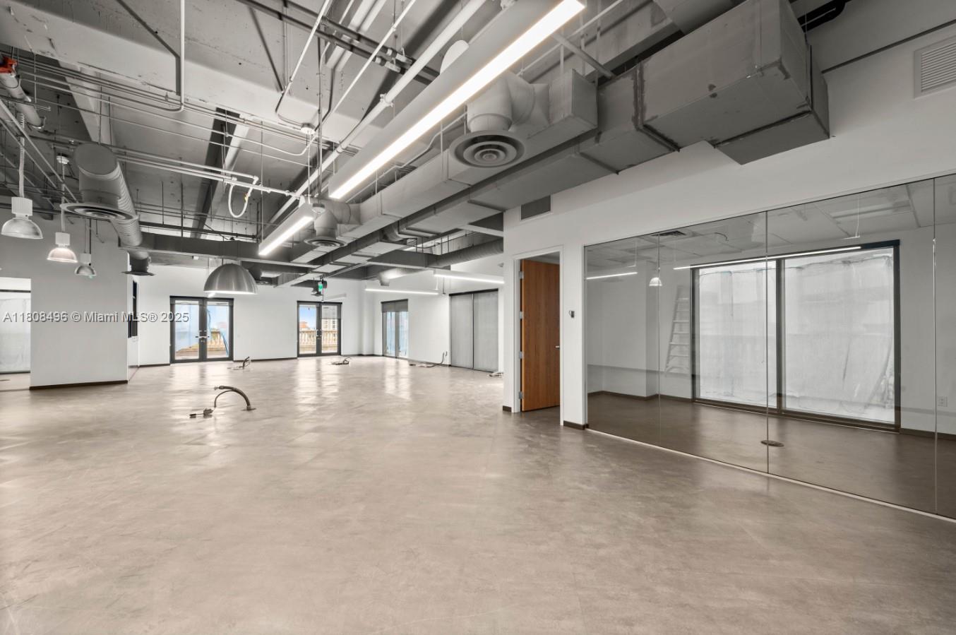 An open-plan office space features polished concrete floors, exposed industrial ceilings, and a glass-enclosed room — 2020 Ponce De Leon Blvd, Coral Gables FL 33134, CORAL GABLES, FL