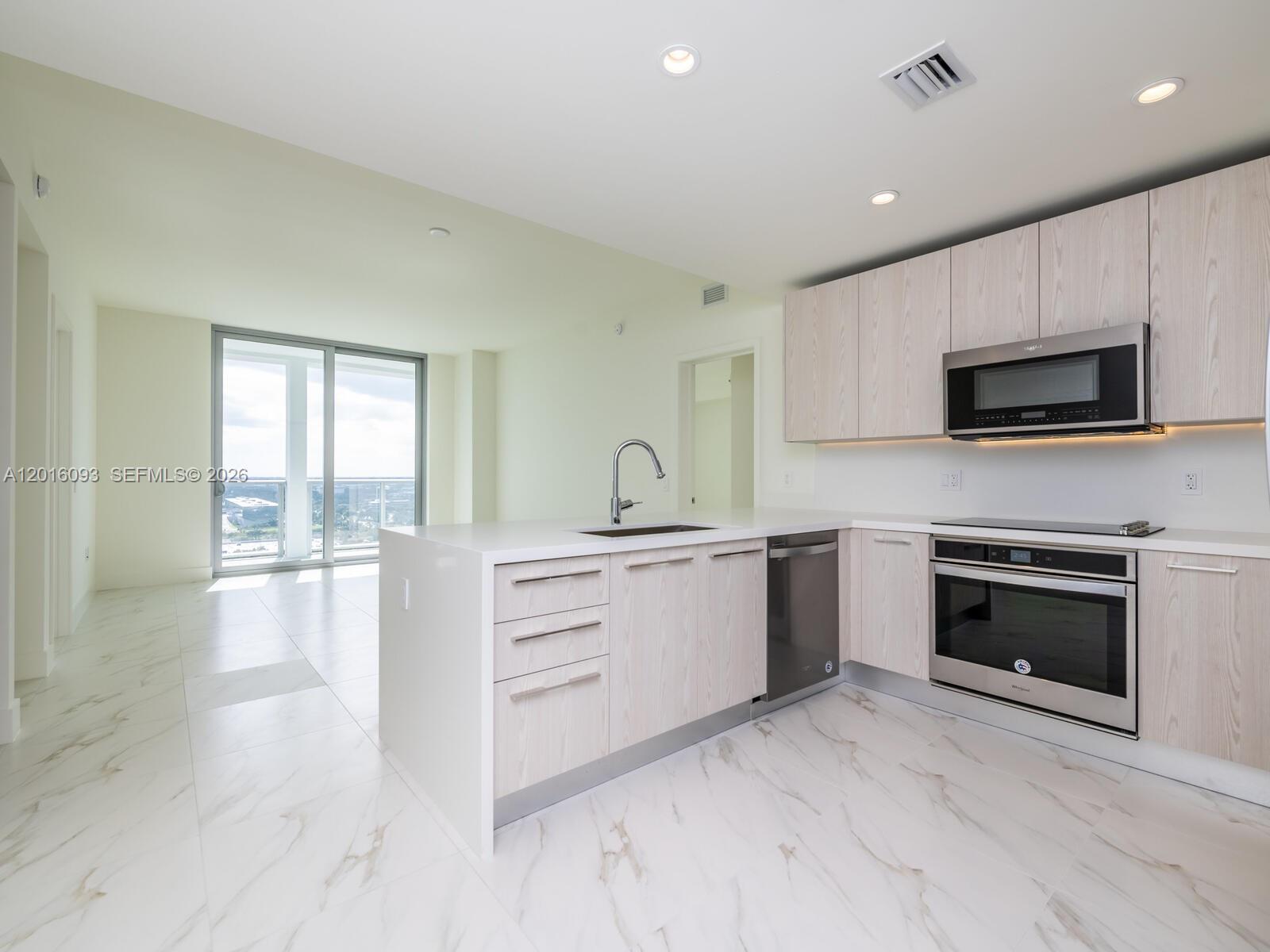 A modern kitchen features light wood cabinets, stainless steel appliances, and white marble-patterned tile floors — 2000 S Metropica Way # 2007, Sunrise FL 33323, SUNRISE, FL