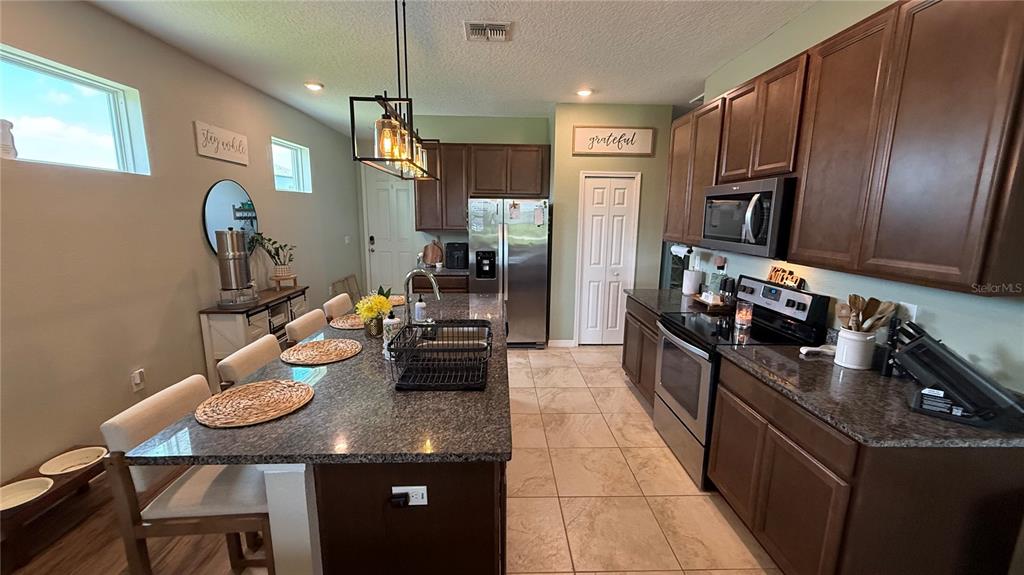 A kitchen features dark wood cabinets, granite countertops, a large island, and tile flooring — 722 LADYFISH LN, NEW SMYRNA BEACH, FL