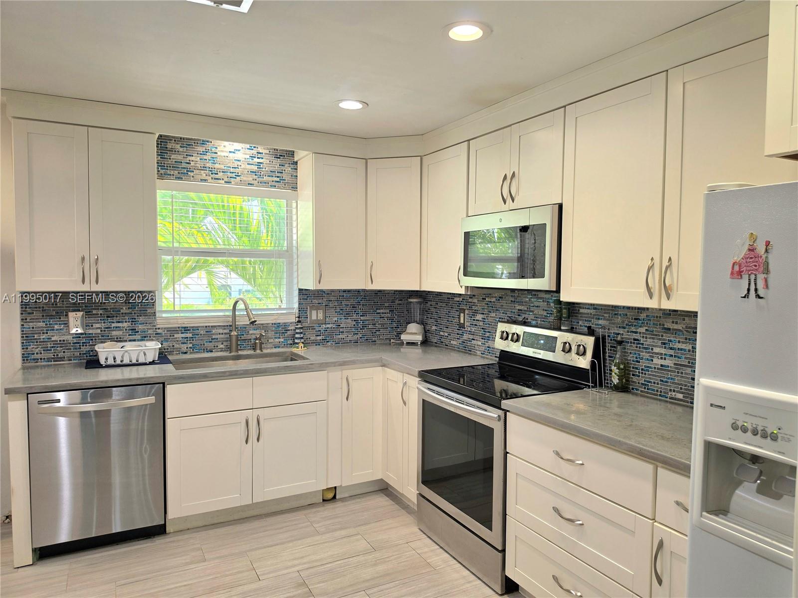 A kitchen features white cabinets, stainless steel appliances, gray countertops, and a blue mosaic backsplash — FORT MYERS, FL