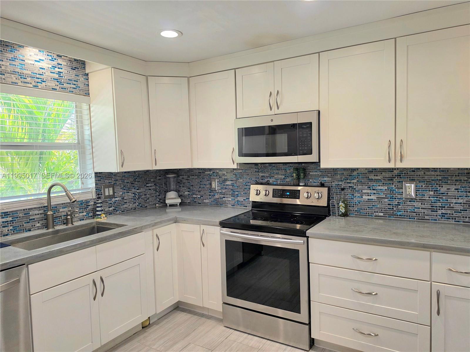 A kitchen features white cabinets, gray countertops, stainless steel appliances, and a blue mosaic backsplash — FORT MYERS, FL