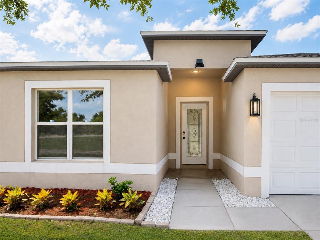 The exterior of a beige house features a front door with glass inlay and landscaping — 5112 LAVAL DRIVE, ORLANDO, FL