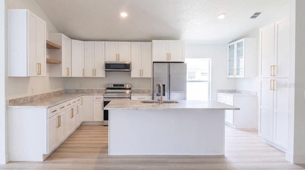A modern kitchen features white cabinets, marble-look countertops, stainless steel appliances, and a central island — 5112 LAVAL DRIVE, ORLANDO, FL