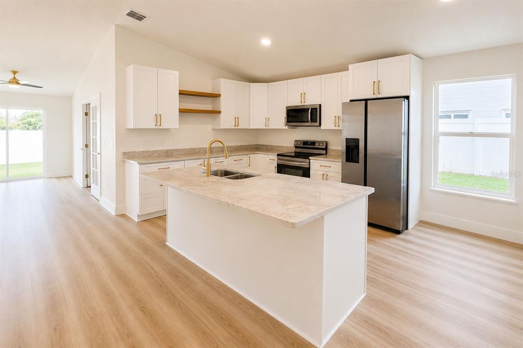 A kitchen features white cabinets, a central island with a sink, and stainless steel appliances — 5112 LAVAL DRIVE, ORLANDO, FL