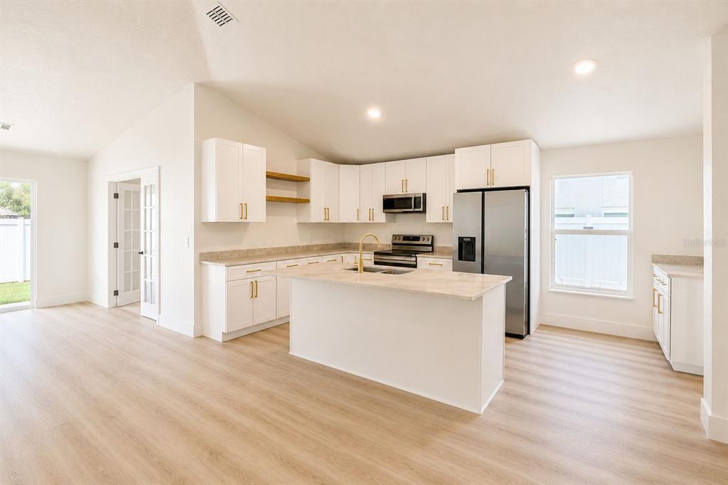 A bright kitchen features white cabinets, a central island, stainless steel appliances, and light flooring — 5112 LAVAL DRIVE, ORLANDO, FL
