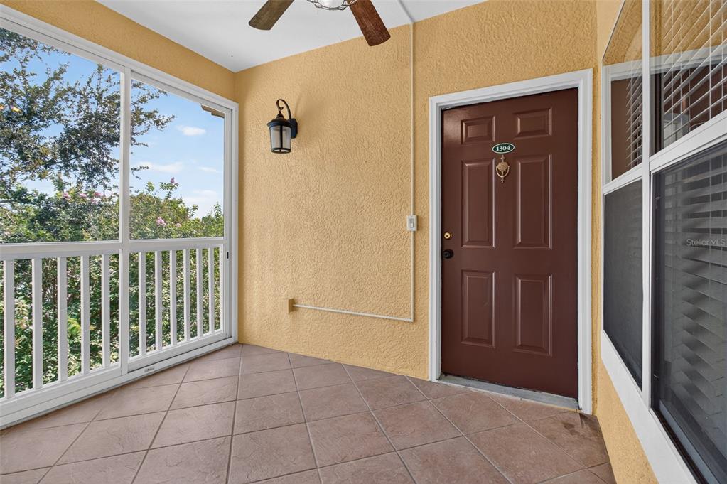 A covered balcony features a brown door, tiled flooring, and a screened-in railing — 10764 70TH AVENUE UNIT 1304, SEMINOLE, FL