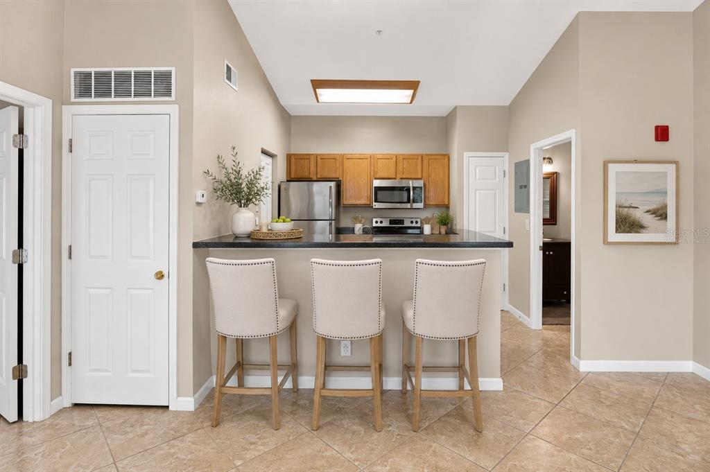 A kitchen with wood cabinets, stainless steel appliances, and a breakfast bar with three chairs — 10764 70TH AVENUE UNIT 1304, SEMINOLE, FL