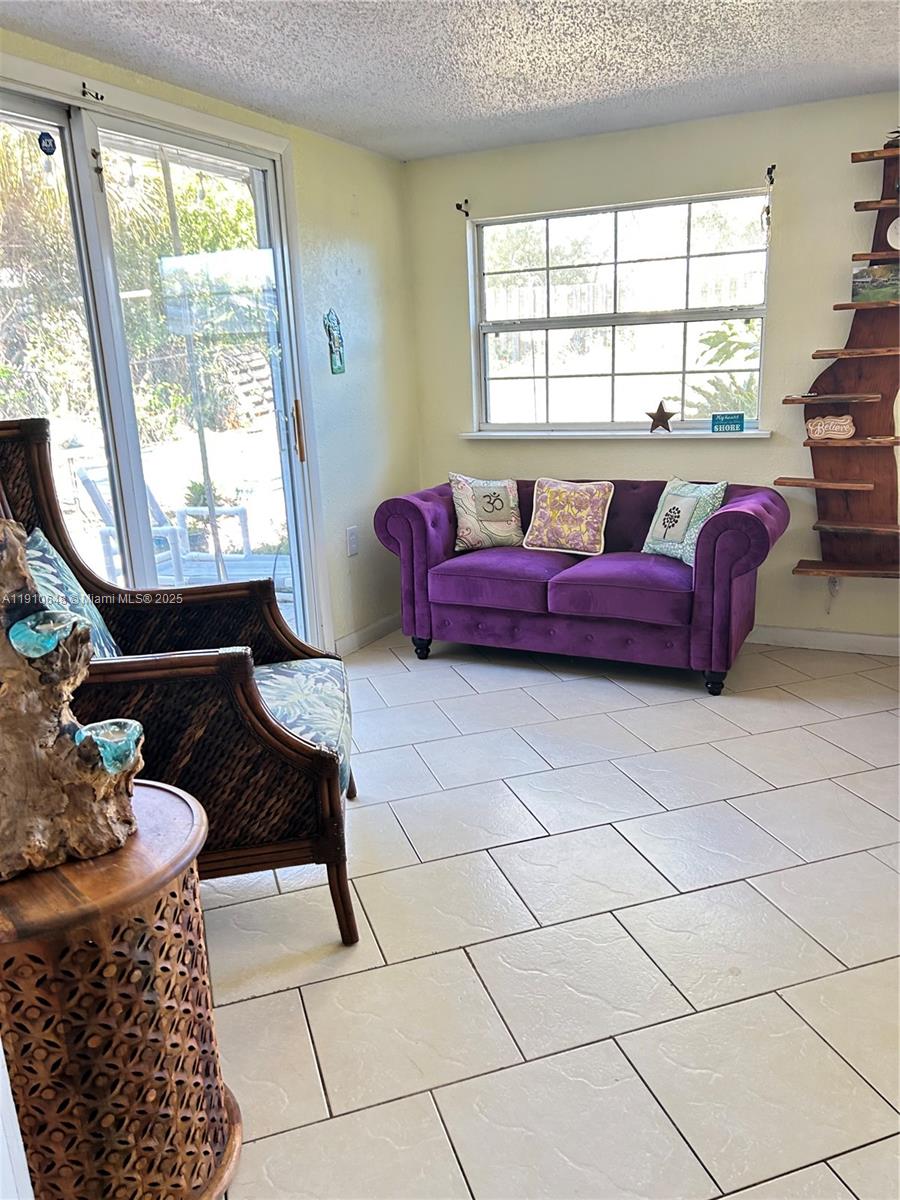A sunroom features a purple tufted sofa, tiled floors, and a sliding glass door — 118 Bougainvillea Dr, Rockledge FL 32955, ROCKLEDGE, FL