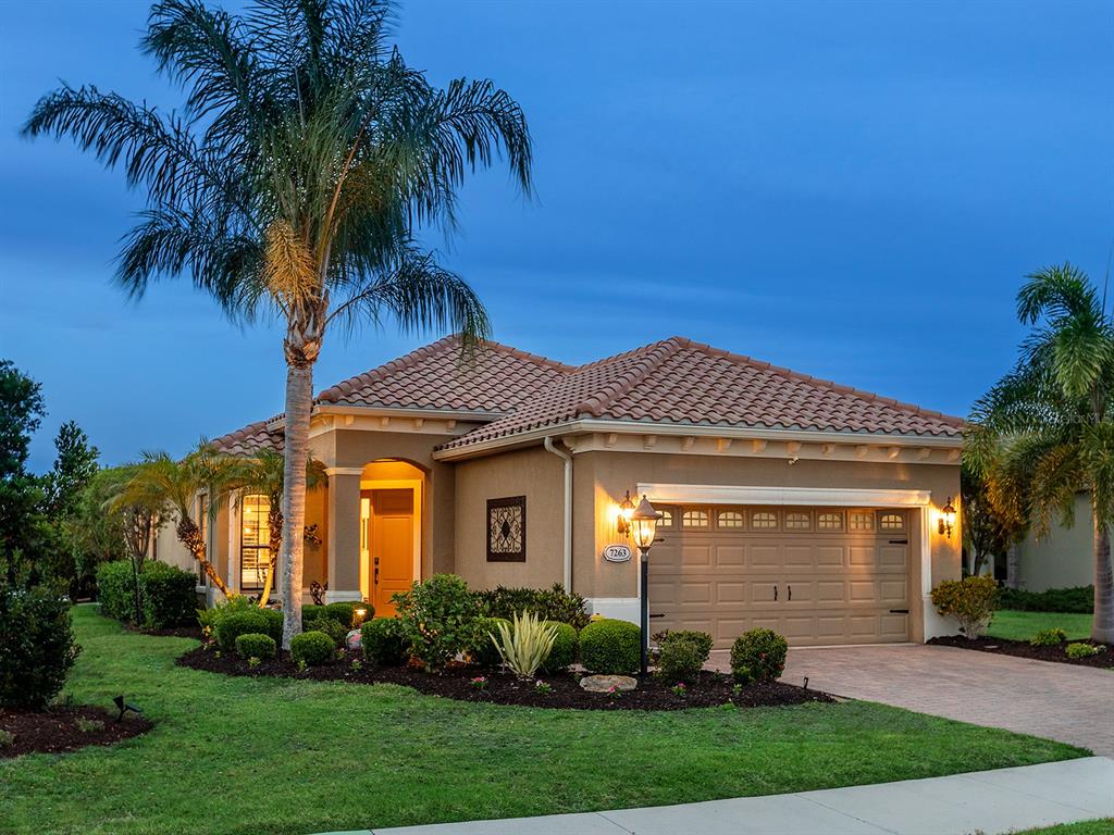 A single-story stucco house with a tiled roof, two-car garage, and palm trees at dusk — 7263 BELLEISLE GLEN, LAKEWOOD RANCH, FL