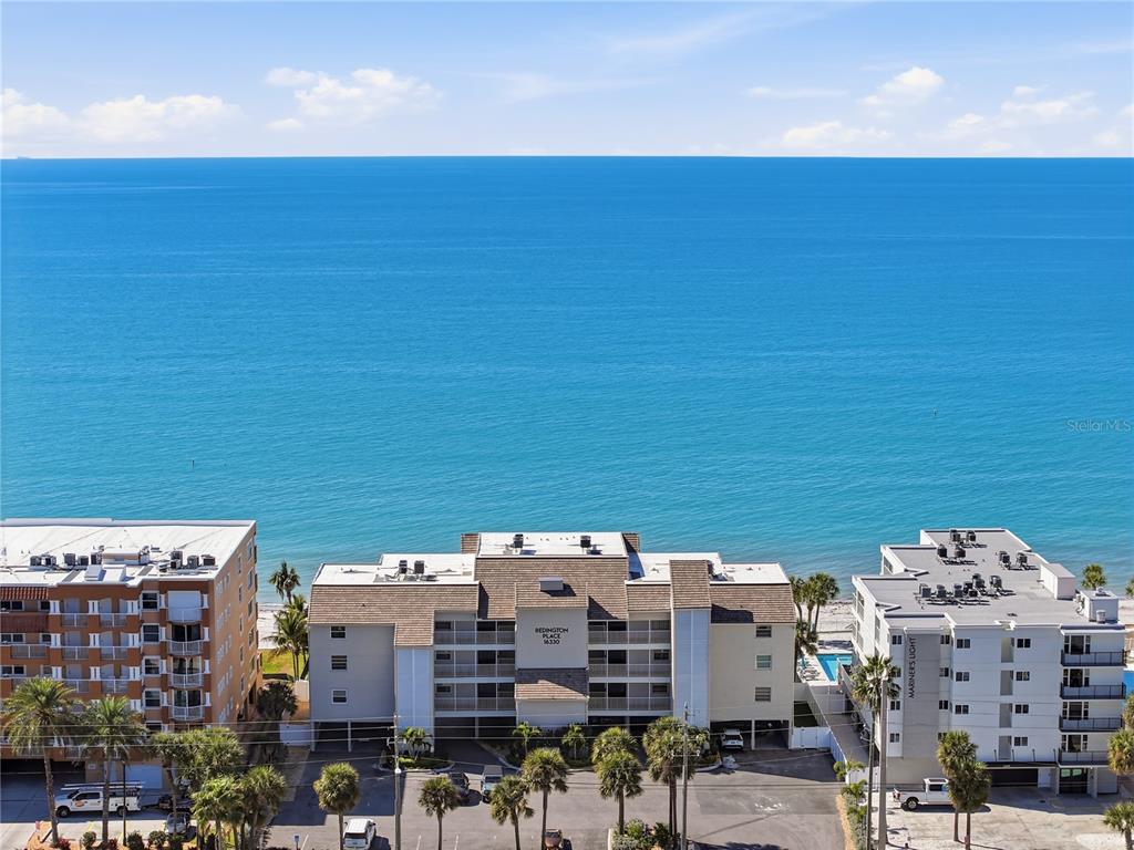 An aerial view shows three beachfront apartment buildings along the coast under a blue sky — 16330 GULF BOULEVARD UNIT 306, REDINGTON BEACH, FL