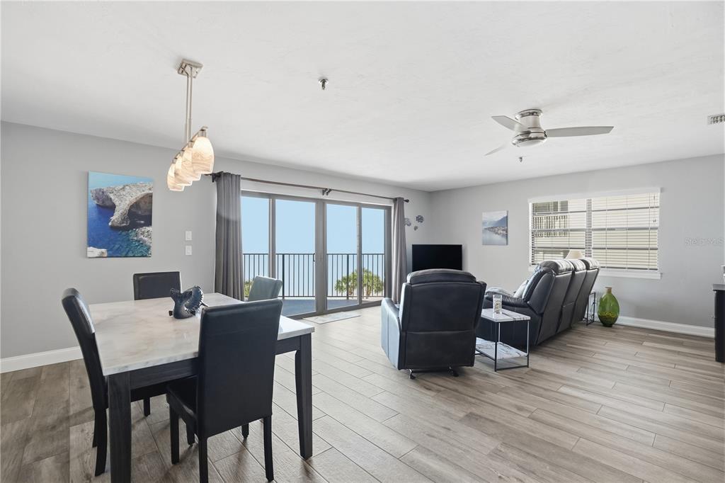 An open-concept living and dining area features light wood-look flooring and a balcony view — 16330 GULF BOULEVARD UNIT 306, REDINGTON BEACH, FL