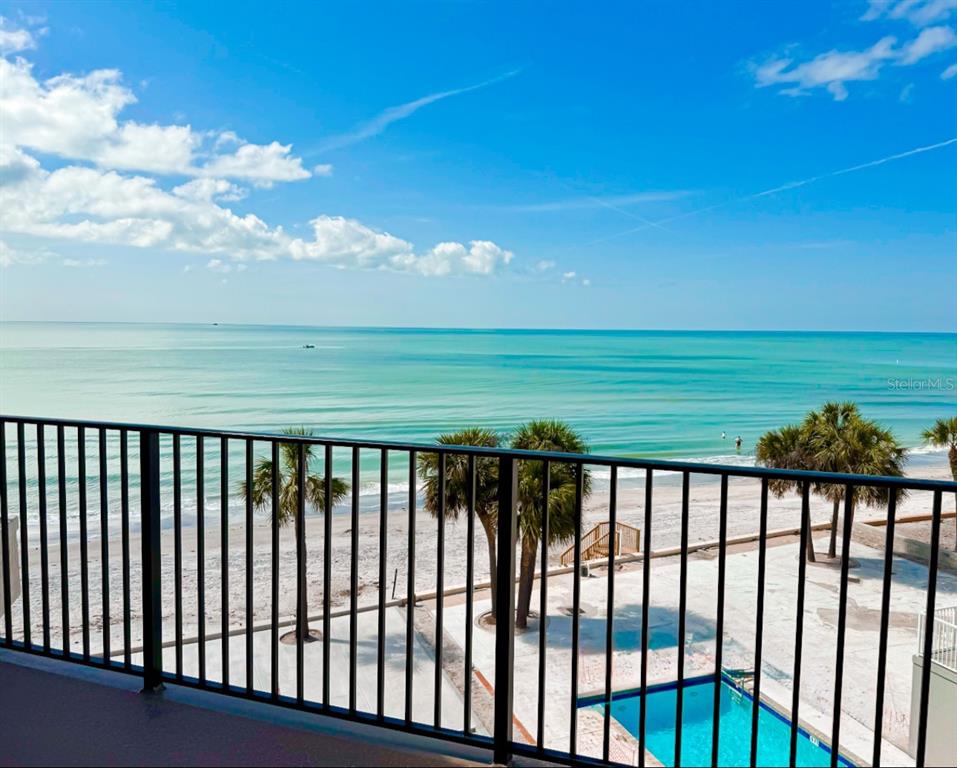 A balcony view overlooks a sandy beach, palm trees, a swimming pool, and the ocean — 16330 GULF BOULEVARD UNIT 306, REDINGTON BEACH, FL