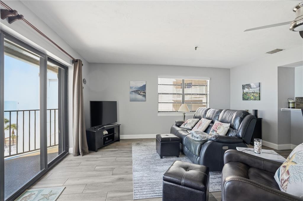 A living room features gray walls, wood-look tile flooring, a leather sofa, and a balcony — 16330 GULF BOULEVARD UNIT 306, REDINGTON BEACH, FL