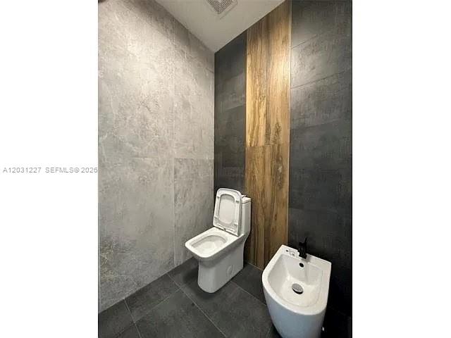 A bathroom features a toilet and bidet against a wall with mixed tile finishes — 8042 NW 114th Pl, Doral FL 33178, DORAL, FL
