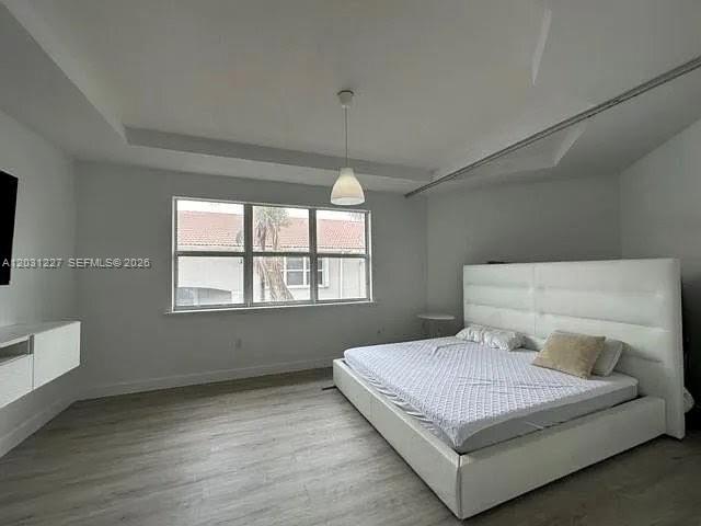 A bedroom features a white tufted bed, light wood flooring, and a tray ceiling — 8042 NW 114th Pl, Doral FL 33178, DORAL, FL