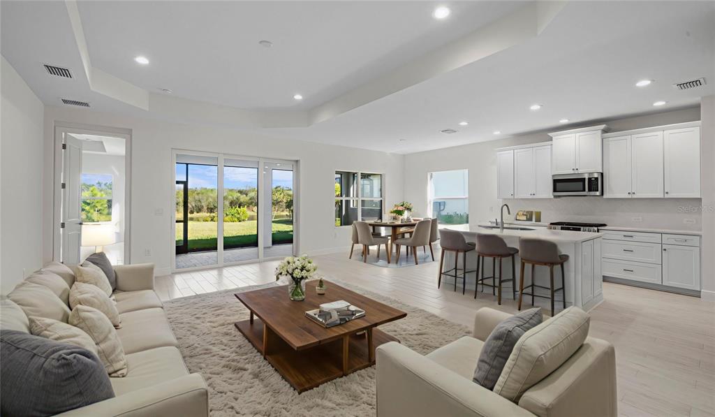 An open-concept living room and kitchen with white cabinetry, a center island, and sliding doors — 13411 HERITAGE PRESERVE DRIVE, FORT MYERS, FL
